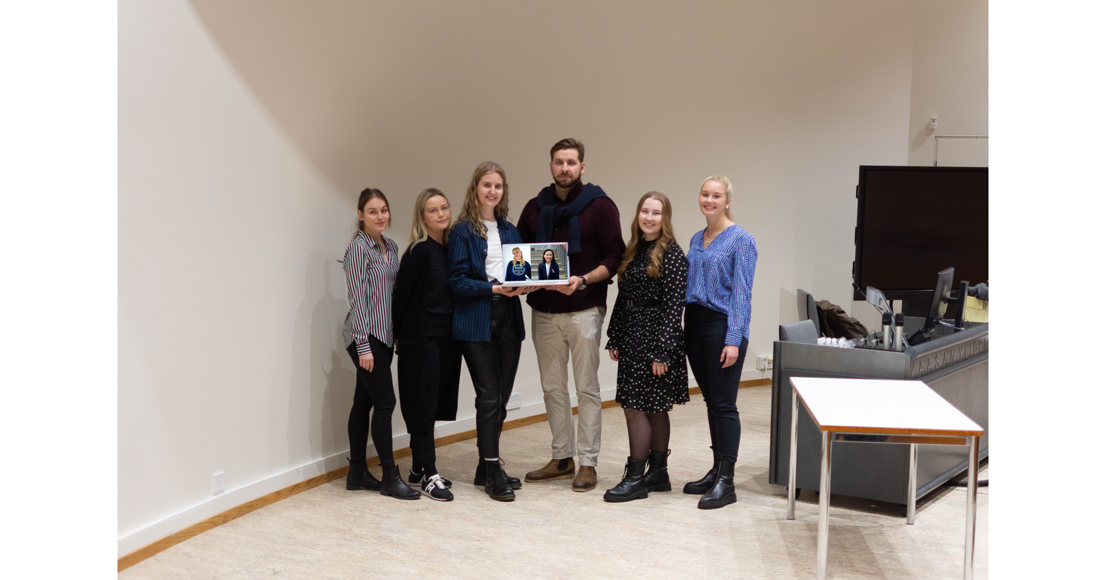 Kuusi vuoden 2022 hallituslaista rivissä ja kaksi henkilöä pitelee kädessään kannettavaa tietokonetta, joissa kahden hallituslaisen kuvat.