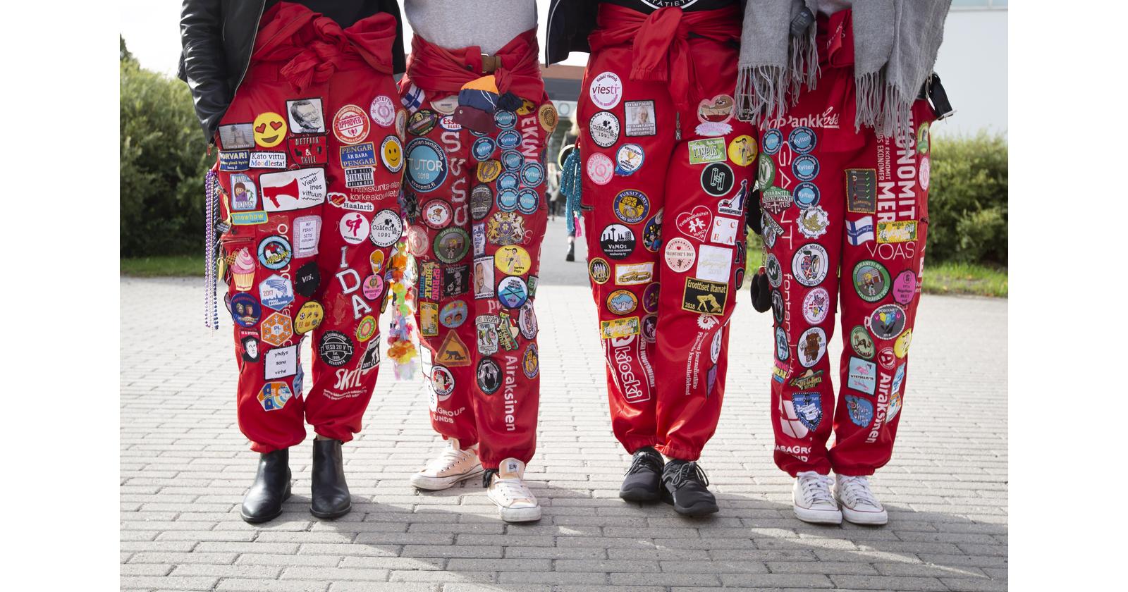 Four students standing at campus wearing red student overalls