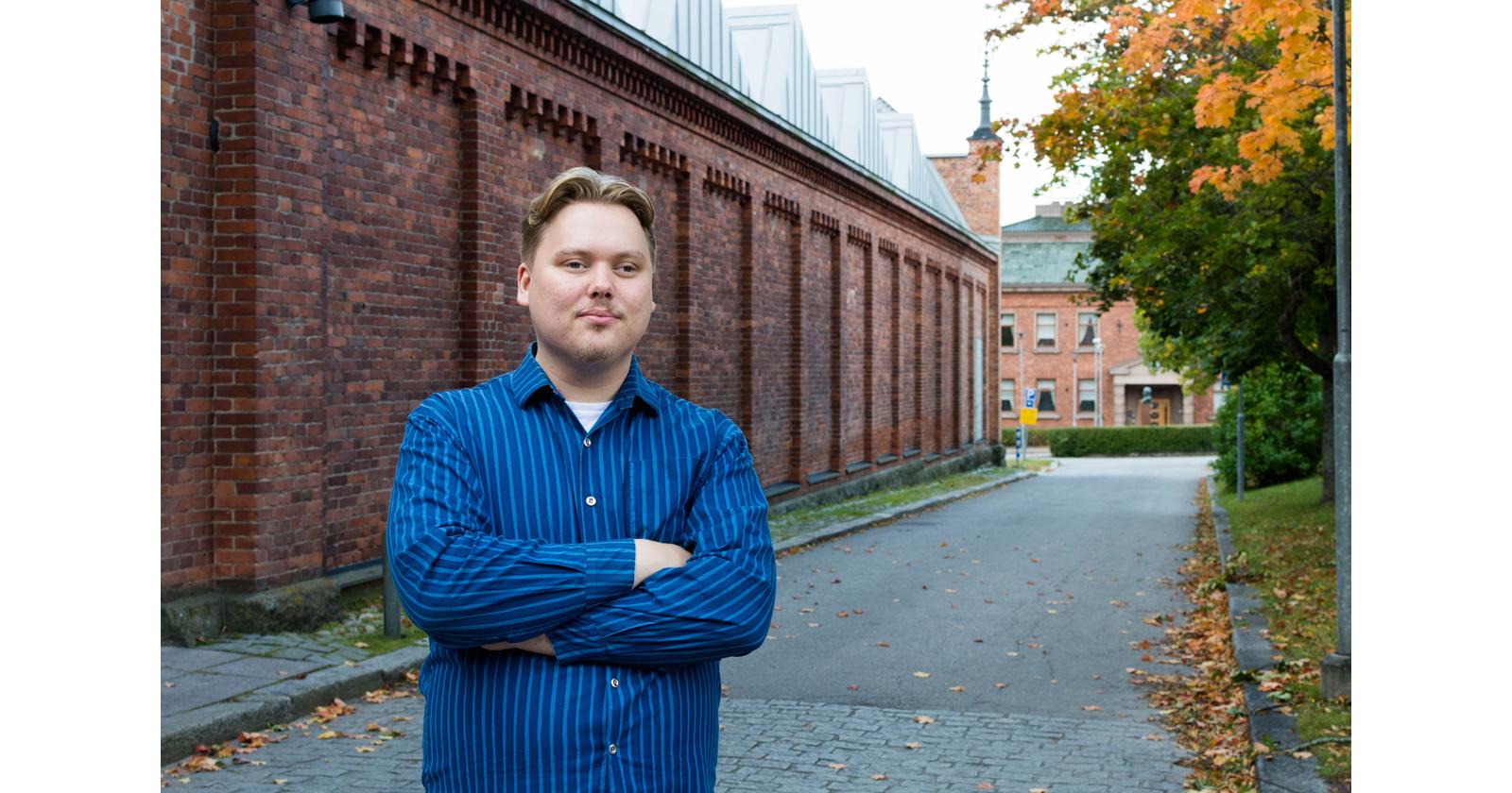 Aleksi Sandroos seisoo Vaasan yliopiston kampuksella tiiliseinän edessä