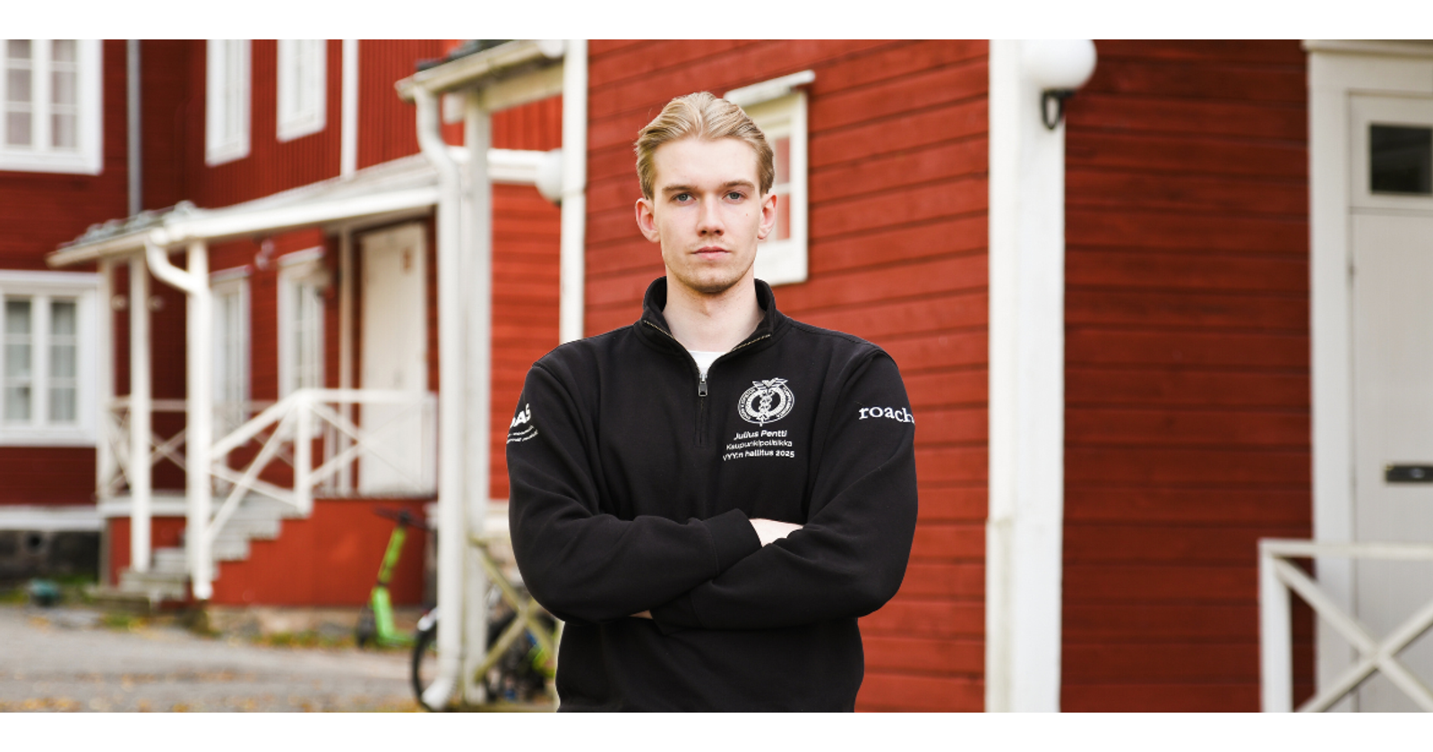 Julius Pentti seisoo kampuksen punasein&auml;isten opiskelija-asuntojen edess&auml;. H&auml;n on ristinyt k&auml;tens&auml; rinnalle ja katsoo vakavana kameraan. H&auml;nell&auml; on yll&auml;&auml;n VYY:n hallituksen collegepaita, josta k&auml;y ilmi h&auml;nen teht&auml;v&auml;ns&auml; kaupunkipoliittisena vastaavana.