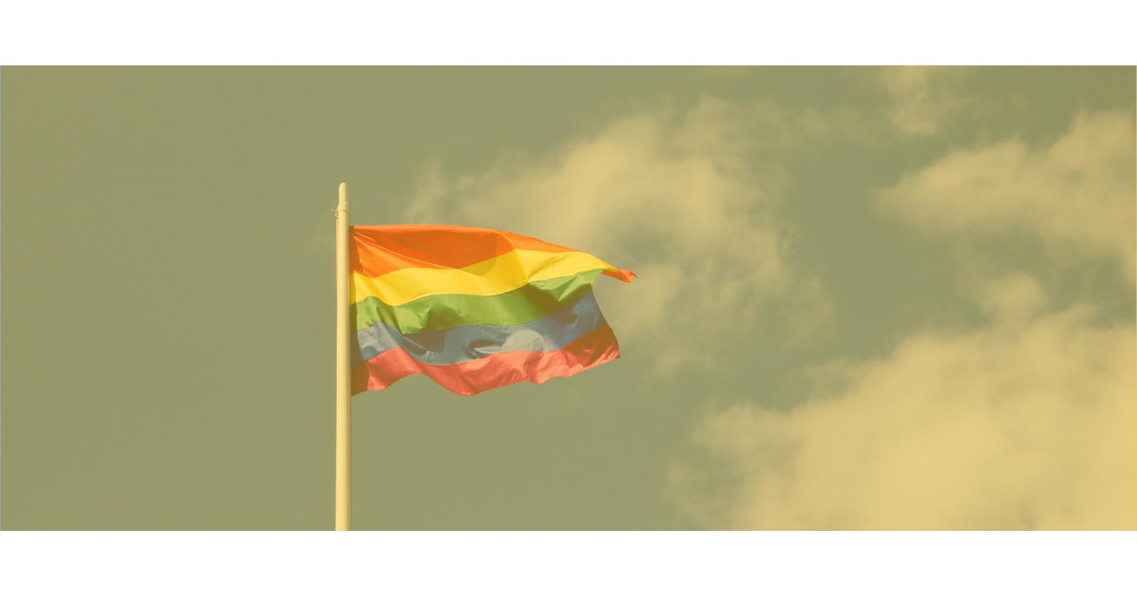 Sateenkaarilippu liehumassa sinisellä taivaalla. Kuva sävyltään keltainen.