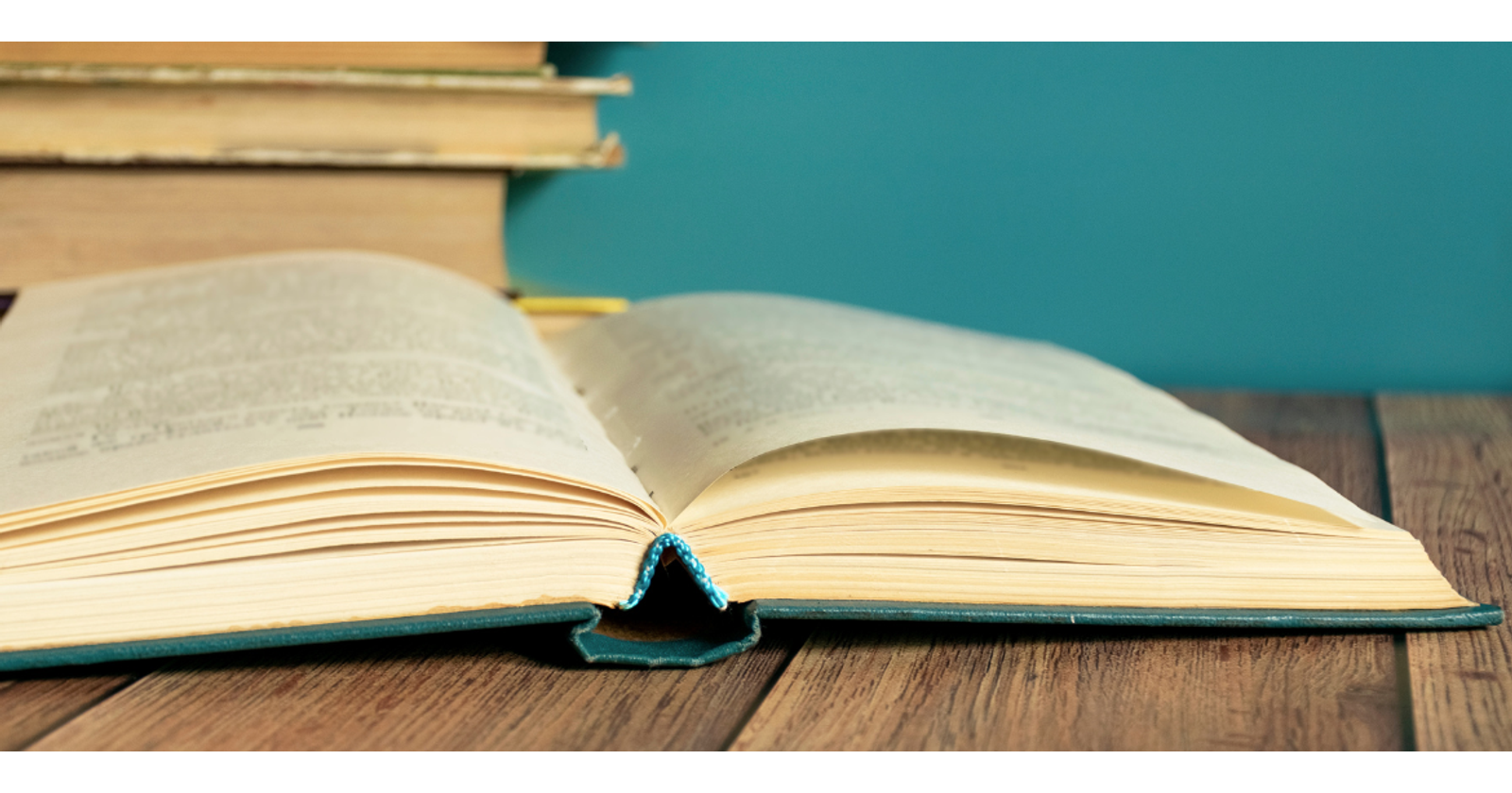 Photograph of an open book with a stack of books in the background and a turquoise wall.
