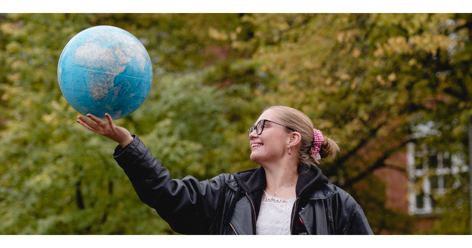Valokuvassa nuori nainen pitää kädessään suurta maapalloa.