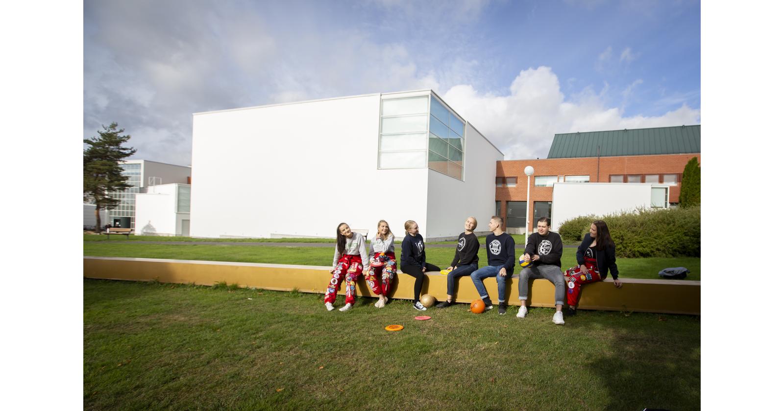 Seven happy students sitting at campus smiling