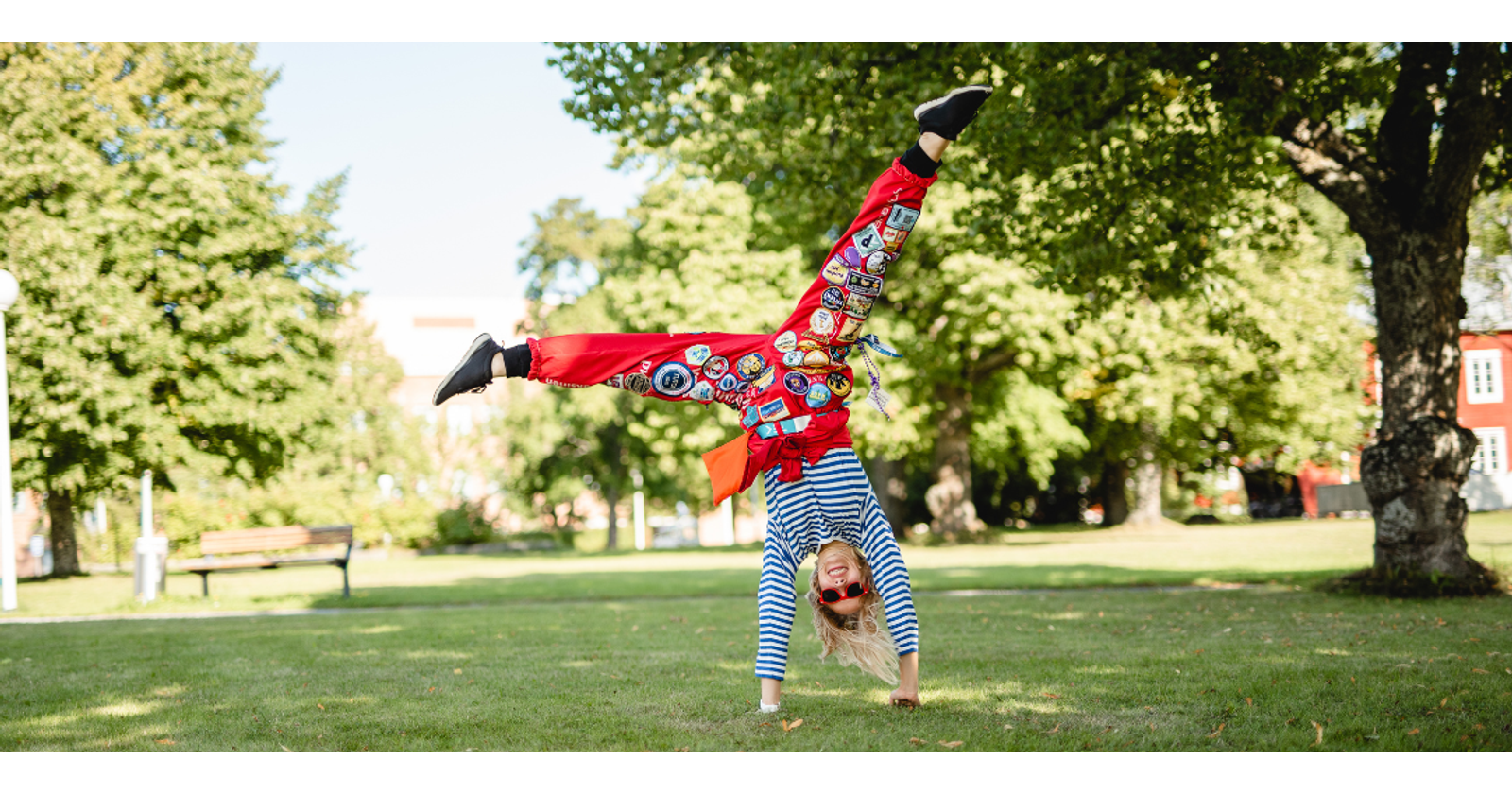 Valokuvassa nuori nainen opiskelijahaalareissa heittää kärrynpyörää aurinkoisena päivänä nurmikolla.