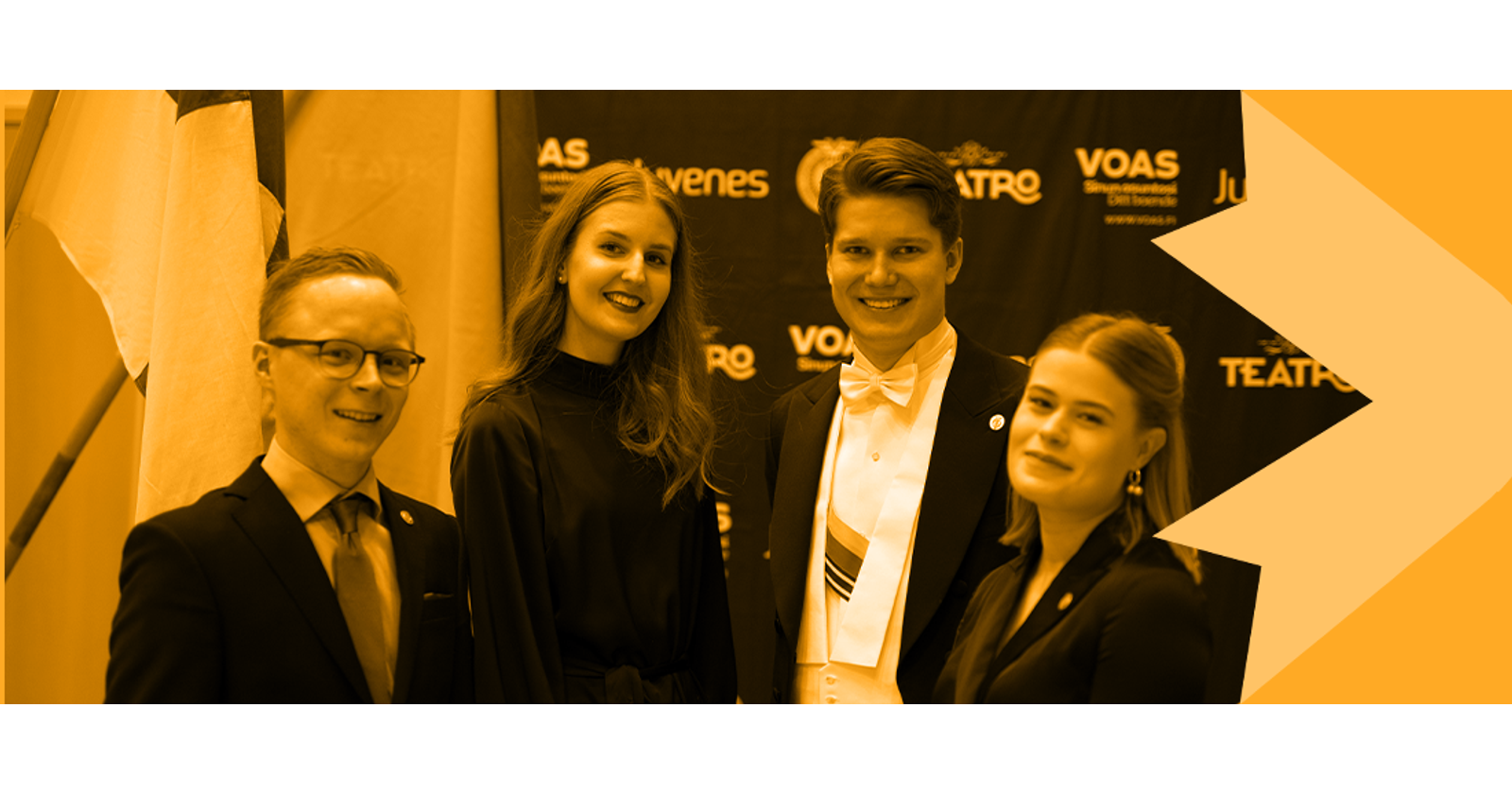 Yhteisösektorin Olli, Sara, Henri ja Aada poseeraavat Suomen ja ylioppilaskunnan lipun edessä vuosijuhlilla