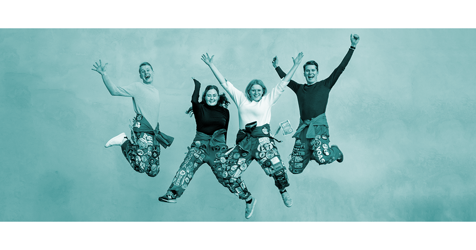 Neljä opiskelijaa opiskelijahaalareissa hyppää iloisesti