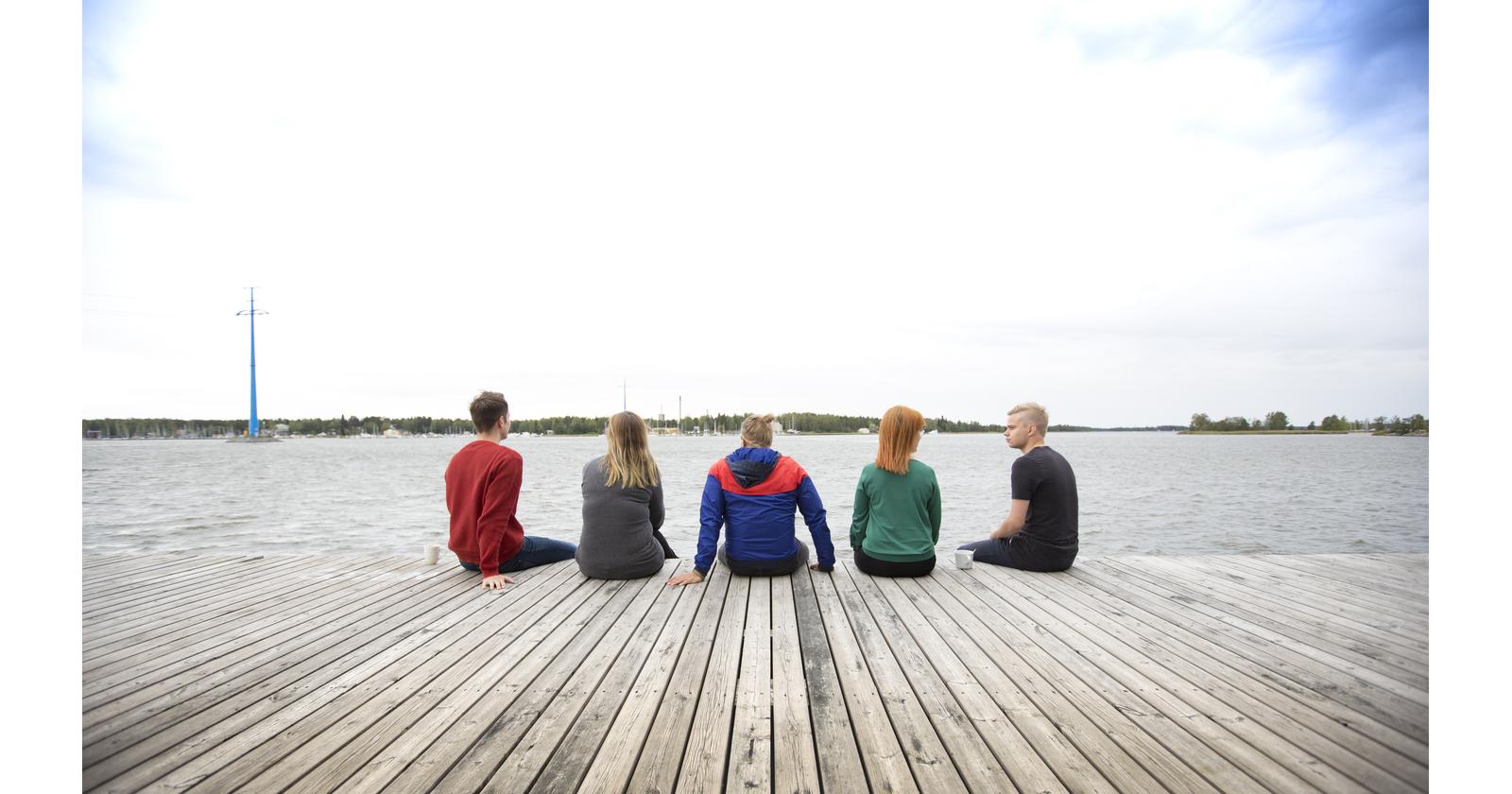 Viisi henkilöä istuu laiturilla ja katsoo merelle