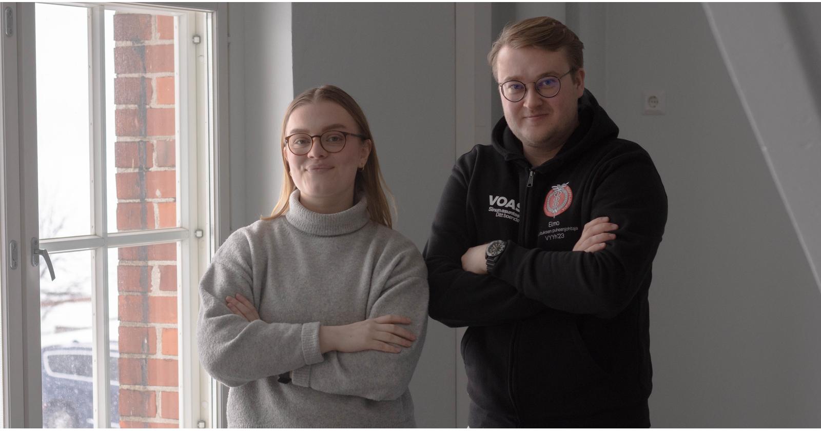 Laura ja Elmo seisovat valottuneen ikkunan vieressä kädet ristissä.