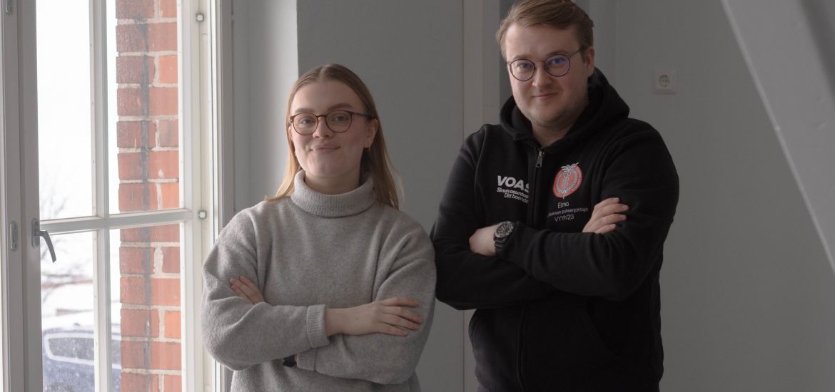 Laura and Elmo standing next to a window with their arms crossed