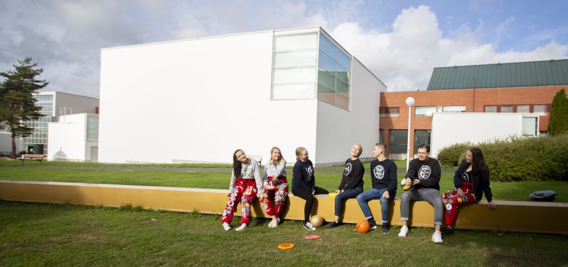 Seven happy students sitting at campus smiling