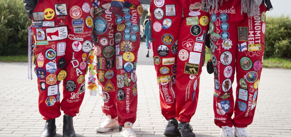 Four students standing at campus wearing red student overalls