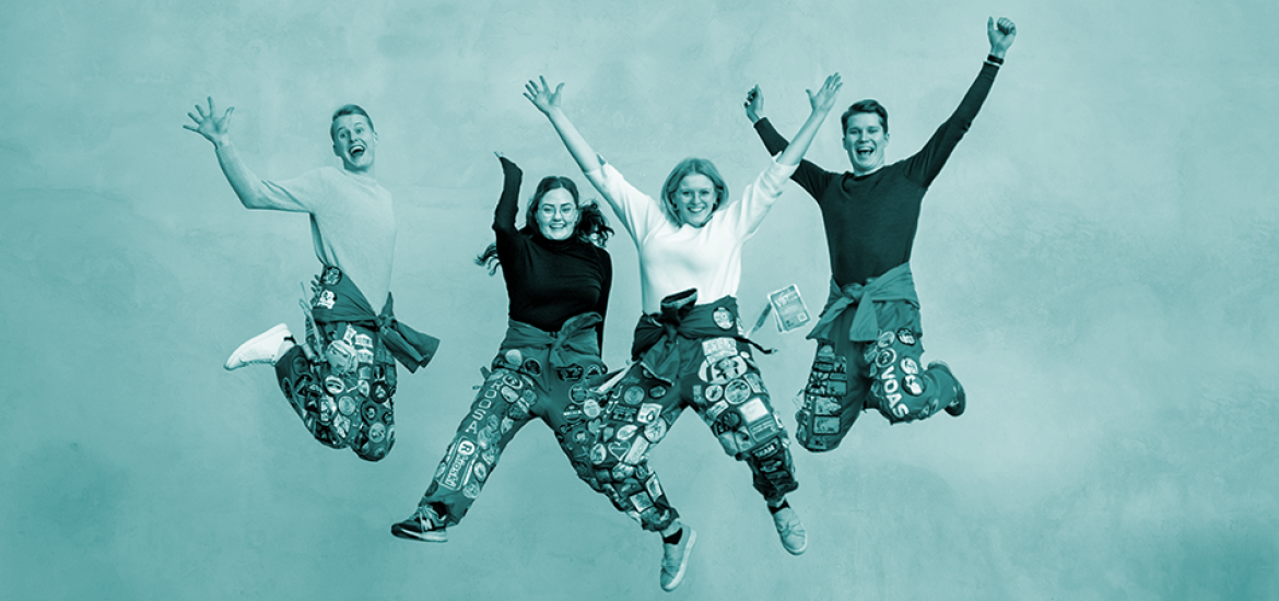 Four students wearing student overalls jumping up in the air happily